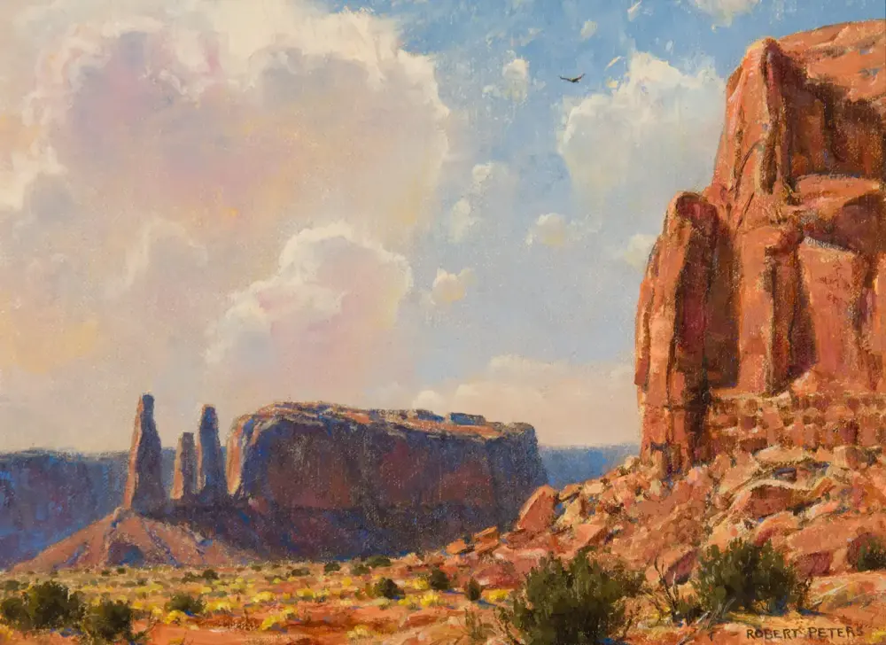 Desert landscape with red rock cliffs, scrubby vegetation, and a blue sky overhead.