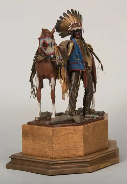 Beaded Native American rider wearing a feather headdress beside a horse on a wooden display base.