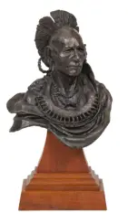Bronze bust of a Native American man with a feathered headdress and beaded necklace, mounted on a wooden pedestal.