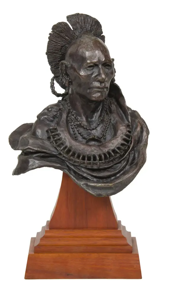 Bronze bust of a Native American man with a feathered headdress and beaded necklace, mounted on a wooden pedestal.