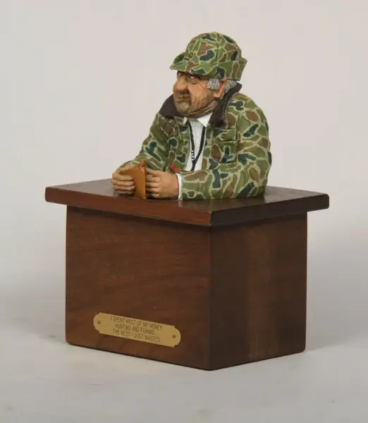 Wooden sculpture of a hunter in camo at a desk, counting money with a humorous plaque on the front reading, 'I spent most of my money hunting and fishing... the rest I just wasted'