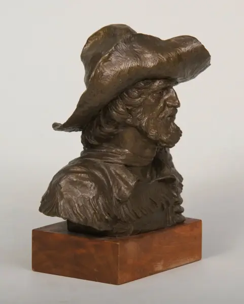 Bronze bust of a bearded man wearing a large wide-brimmed hat on a wooden pedestal.