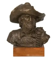 Bronze bust of a rugged cowboy with a wide-brimmed hat and beard, mounted on a wooden plinth.