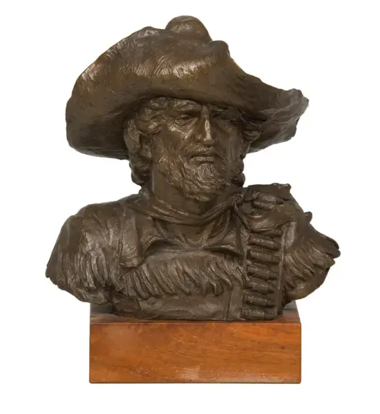 Bronze bust of a rugged cowboy with a wide-brimmed hat and beard, mounted on a wooden plinth.