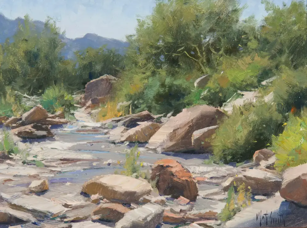 Impressionist landscape: a rocky stream with water weaving around large stones and lush green trees in the background.