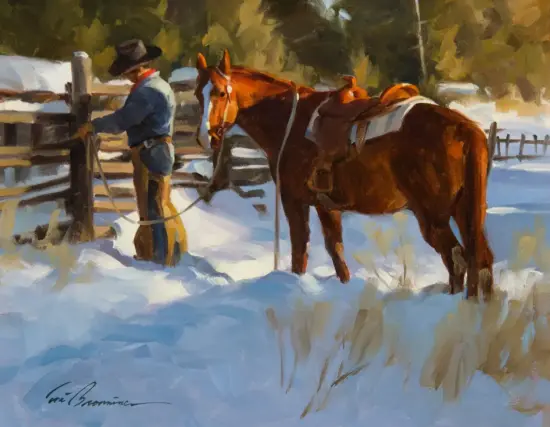 Man in a blue jacket and black hat standing in the snow beside two saddled horses by a wooden fence, winter scene.