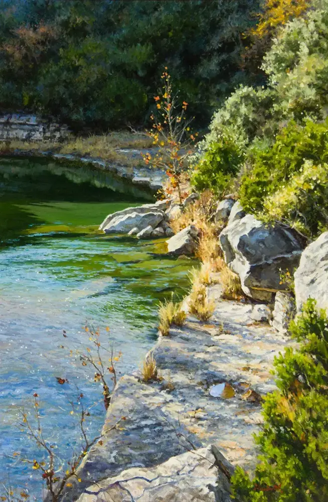 Rocky lakeshore with green shrubs and clear blue-green water along the edge.