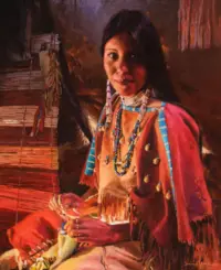 Portrait of a Native American woman in an orange dress with blue bead necklaces, seated beside a loom while weaving beaded jewelry.