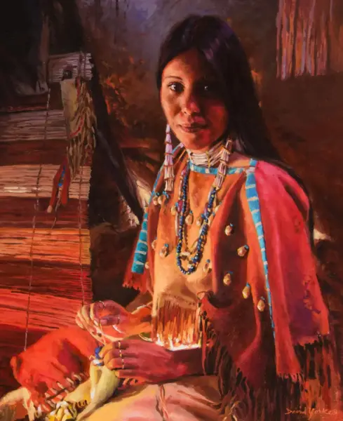 Portrait of a Native American woman in an orange dress with blue bead necklaces, seated beside a loom while weaving beaded jewelry.