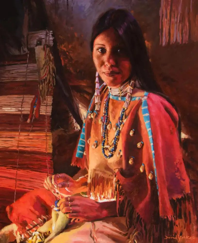 Portrait of a Native American woman in an orange dress with blue bead necklaces, seated beside a loom while weaving beaded jewelry.
