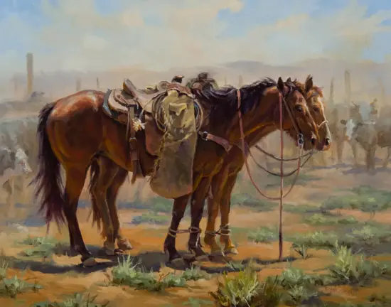 Two saddled horses tied together in a dry, desert landscape with distant fence posts and a vague figure in the background.