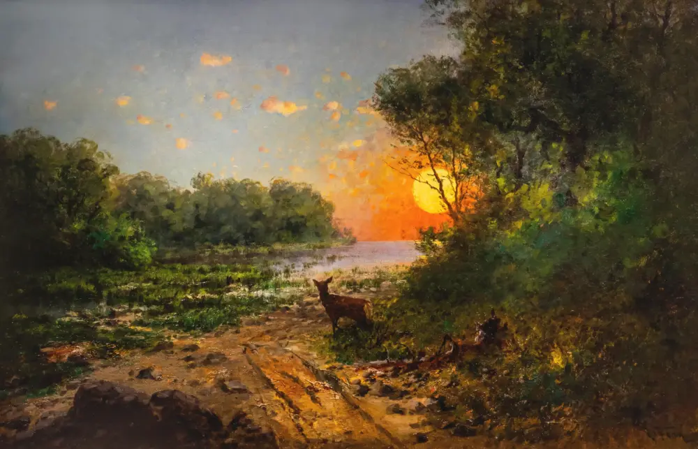 Sunset over a forested riverbank with an orange glow and a deer standing on the shore in the foreground.