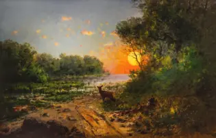 Sunset over a forested riverbank with an orange glow and a deer standing on the shore in the foreground.