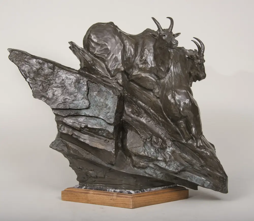 Bronze sculpture of a bison on a wooden base, shown mid-stride with raised head and curved horns.