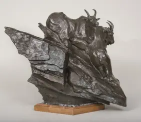Bronze sculpture of a bison on a wooden base, shown mid-stride with raised head and curved horns.